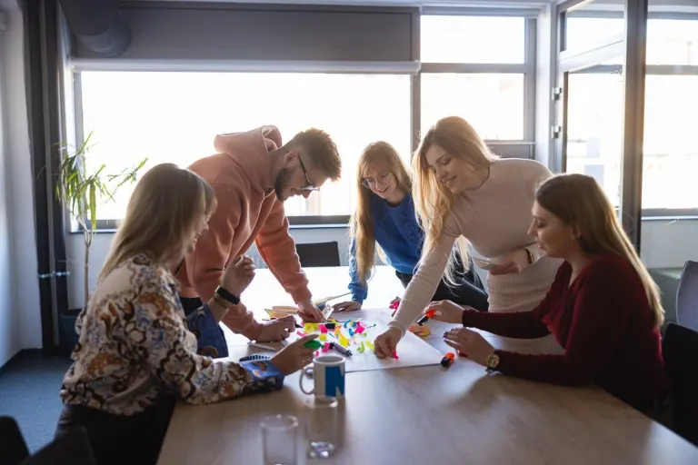 Projektowanie doświadczeń cyfrowych z wykorzystaniem AI | Uniwersytet WSB Merito Szczecin: Grupa studentów wspólnie pracuje nad kreatywnym projektem, używając kolorowych karteczek i markerów.