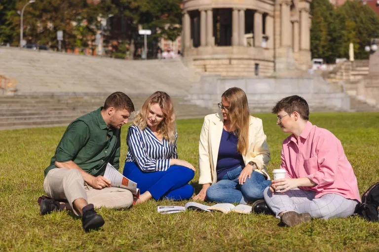 Strategie i techniki sprzedaży | Studia I stopnia w Szczecinie | Uniwersytet WSB Merito Szczecin: Grupa studentów siedzi na trawie i wspólnie uczy się z książek w plenerze.