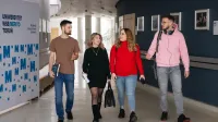 Projektowanie marki i wizerunku firmy | Uniwersytet WSB Merito w Toruniu: Grupa czterech studentów idzie korytarzem uniwersytetu WSB Merito w Toruniu