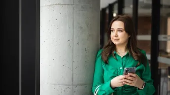 Menedżer przedsiębiorstwa turystycznego | Uniwersytet WSB Merito w Toruniu: Główna grafika: Toruń - studia licencjackie - Studentka w zielonej koszuli pozująca do zdjęcia na korytarzu