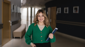 Projektowanie komunikacji i doświadczeń marki | Uniwersytet WSB Merito w Toruniu: Studentka WSB Merito na korytarzu uczelni trzyma książkę w ręku