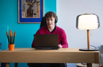 Aktualności | Uniwersytet WSB Merito w Toruniu: student przed laptopem ze słuchawkami na głowie