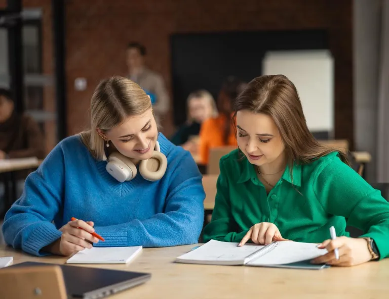 Kierunki inżynierskie - mniejsza inwestycja, ten sam zwrot! | Uniwersytet WSB Merito w Toruniu: dwie studentki przy biurku, współpraca