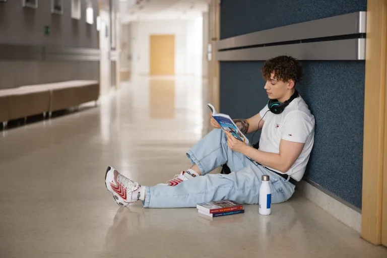 Poznaj nas | Uniwersytet WSB Merito w Toruniu: Główna grafika: Toruń - studia I stopnia - student siedzący na korytarzu