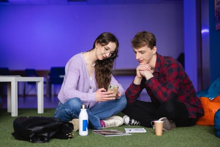 Kompetentna administracja – silne fundamenty nowoczesnej uczelni | Uniwersytet WSB Merito w Toruniu: studenci siedzą, oglądają coś na smartfonie