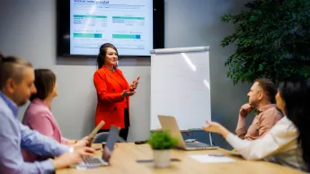 Kadry i płace | Uniwersytet WSB Merito Warszawa: kobieta omawiająca projekt wśród grupy ludzi