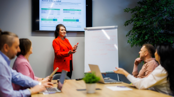 Agile – zwinne metodyki zarządzania projektami | Studia podyplomowe w Warszawie | Uniwersytet WSB Merito Warszawa: kobieta omawiająca projekt wśród grupy ludzi