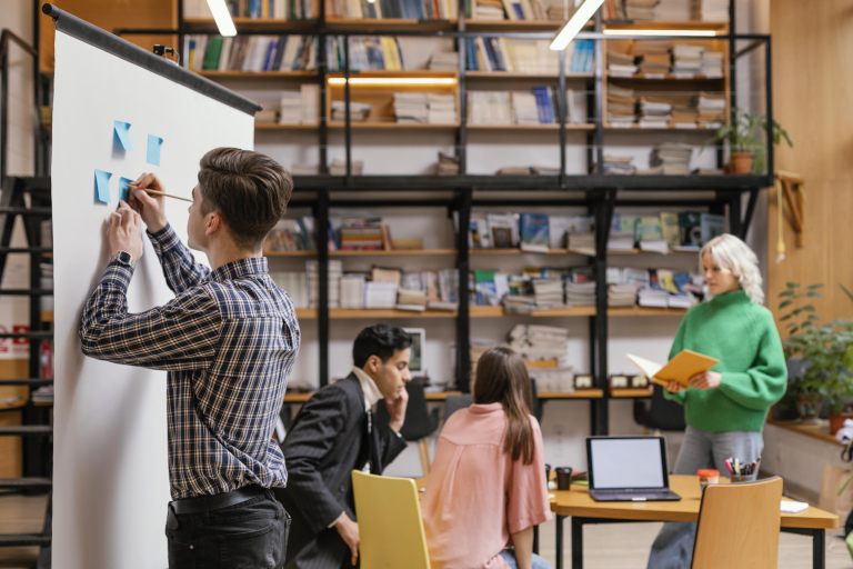 Zarządzanie kryzysowe | Studia podyplomowe we Wrocławiu | Uniwersytet WSB Merito we Wrocławiu: Mężczyzna zapisuje pomysły na tablicy, inni pracują razem przy stole