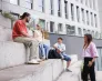 Poznaj nas | Uniwersytet WSB Merito we Wrocławiu: Grafika główna: sekcja poświęcona maturzystom - czwórka studentów siedzi na schodach przy budynku uczelni i rozmawiają