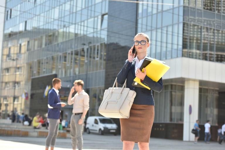 Relacje z biznesem w praktyce | Uniwersytet WSB Merito we Wrocławiu: Kobieta w stroju formalnym z dokuemntami, rozmawia przez telefon na mieście